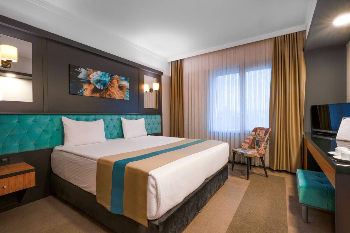 A hotel room with a large bed, a desk with a chair, a TV, and a window with curtains.