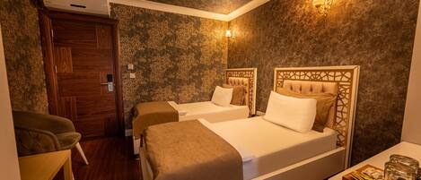 A hotel room with two beds, a wooden door, a small table, and a wall-mounted light fixture.