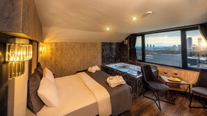 Habitació d'hotel amb un llit, una taula de treball, una cadira, una banyera i vista a la ciutat.