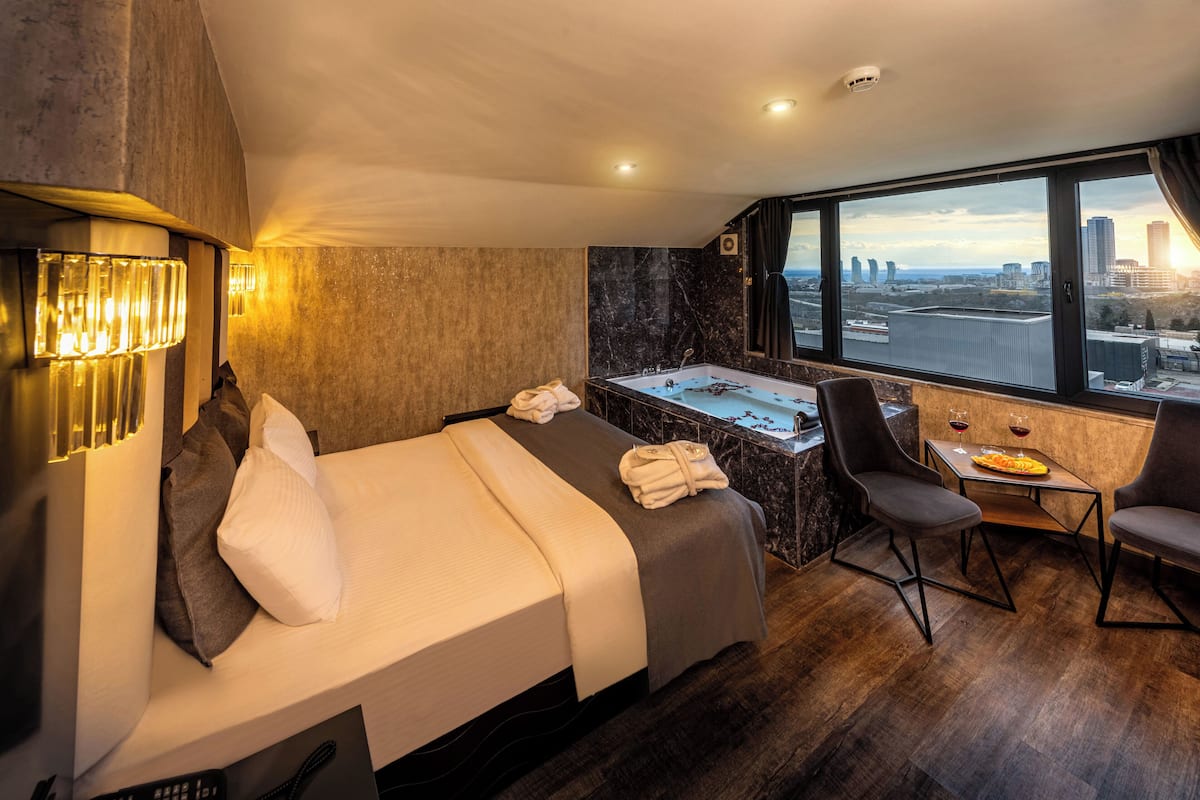 A hotel room with a bed, a desk, a chair, a bathtub, and a city view.