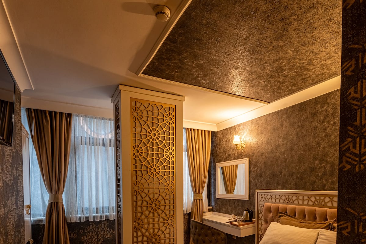 A hotel room with a bed, a desk, a chair, a radiator, and a window with curtains.