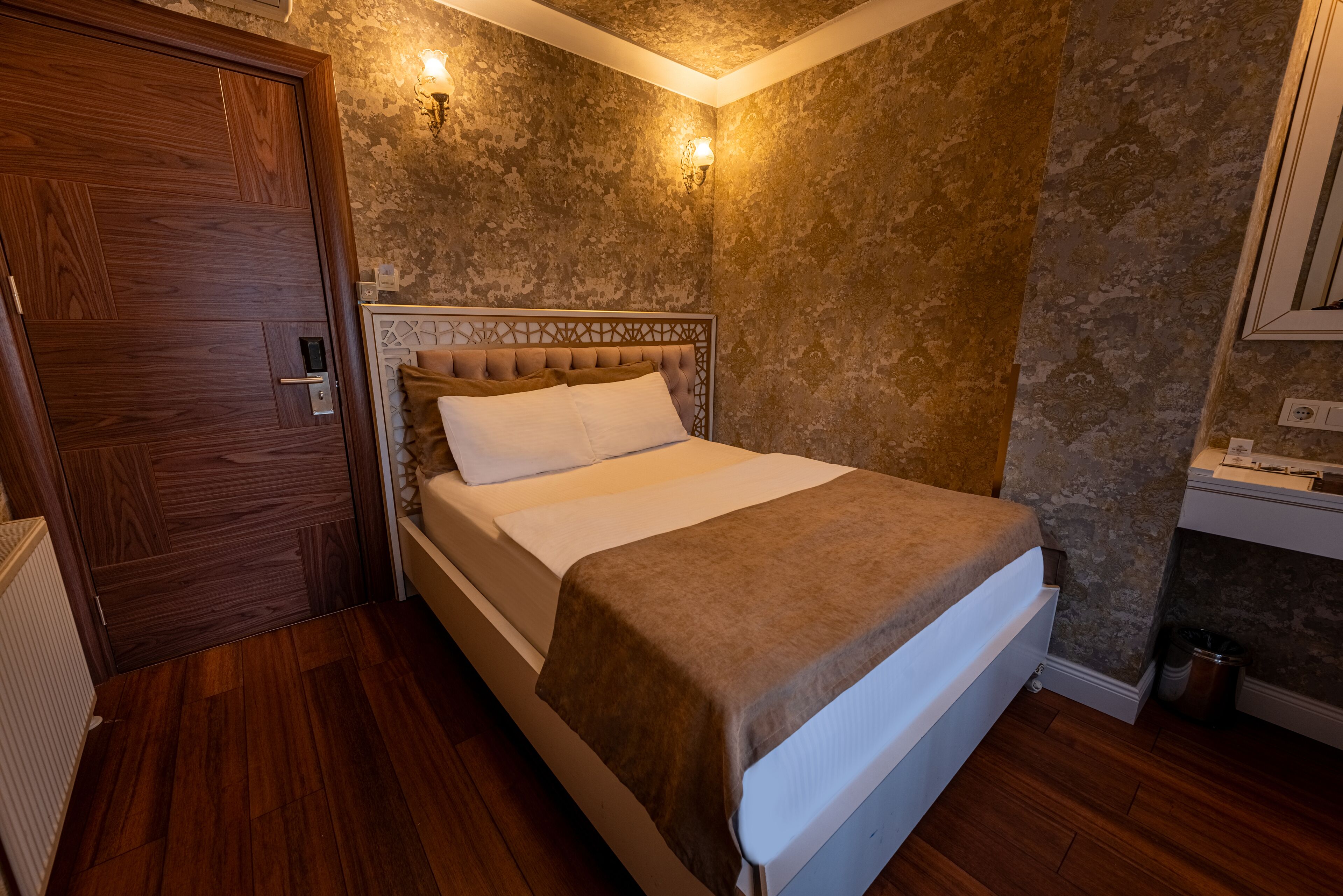 A bedroom with a wooden door, a bed with a beige headboard, and textured walls.