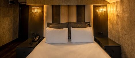 Una camera d'albergo con un letto grande, due comodini, un telefono e lampade a parete.