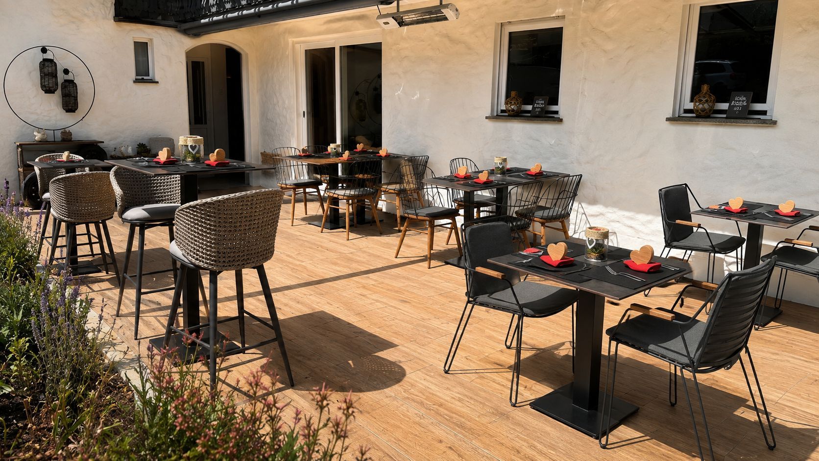 Zona pranzo all'aperto con diversi tavoli e sedie, circondata da un edificio rustico con ampie finestre.