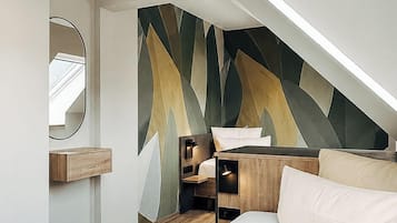 Un dormitorio moderno con techo inclinado, una cama, una mesita de noche, un espejo y una pared con estampado geométrico.