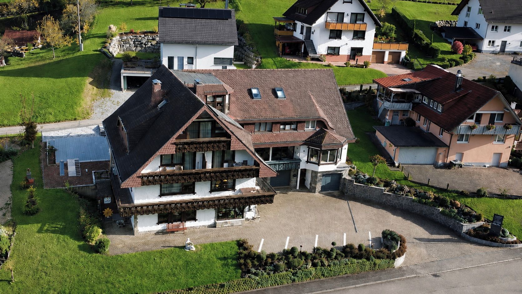 Ein großes Haus mit geneigtem Dach, zahlreichen Fenstern und einer gepflasterten Auffahrt.