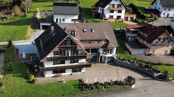 Ein großes Haus mit geneigtem Dach, zahlreichen Fenstern und einer gepflasterten Auffahrt.