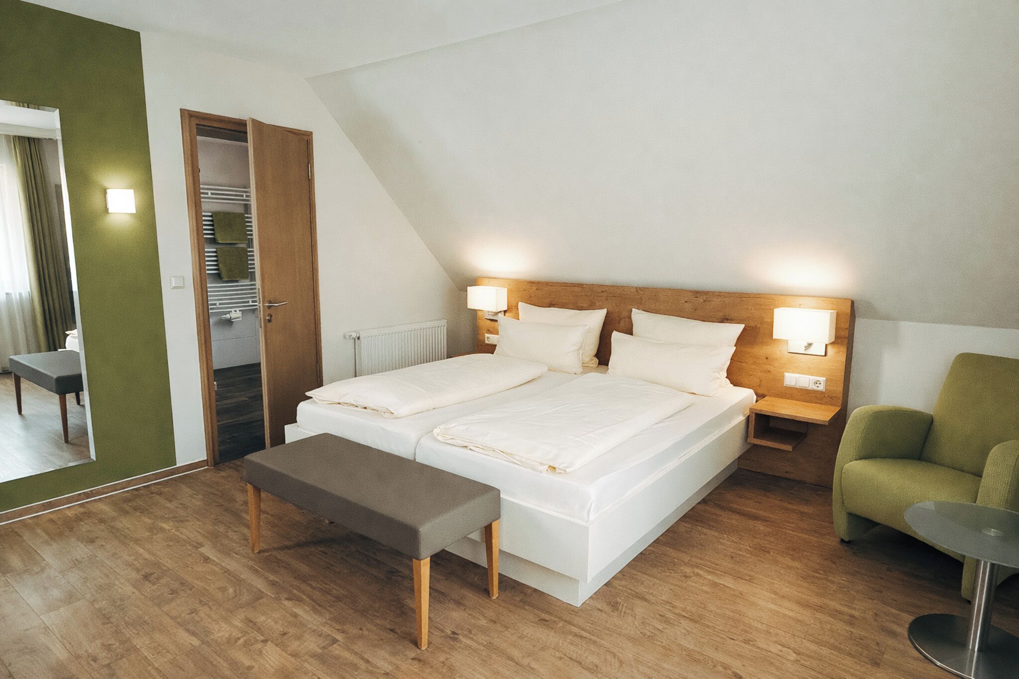 Une chambre à coucher comprenant un lit, des tables de chevet, un banc, une chaise et un miroir.