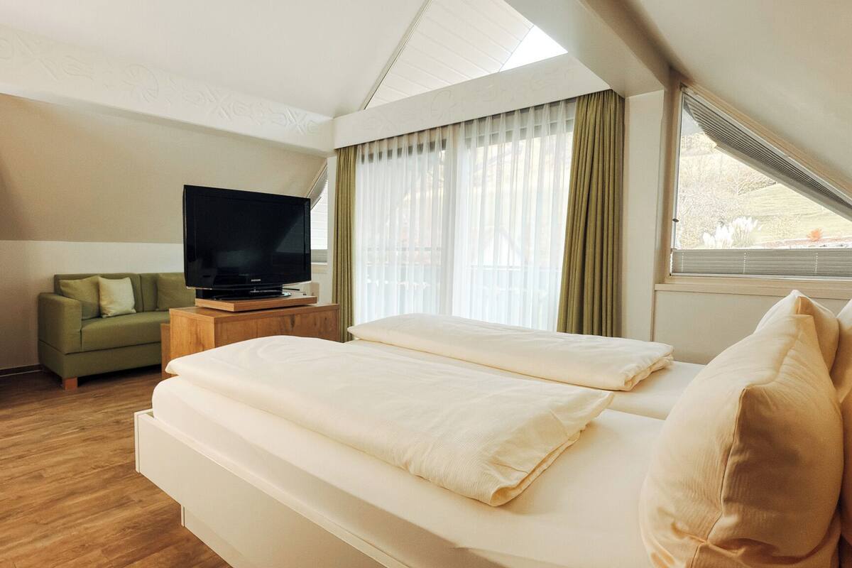 A hotel room with a bed, a television, a sofa, and a wardrobe.