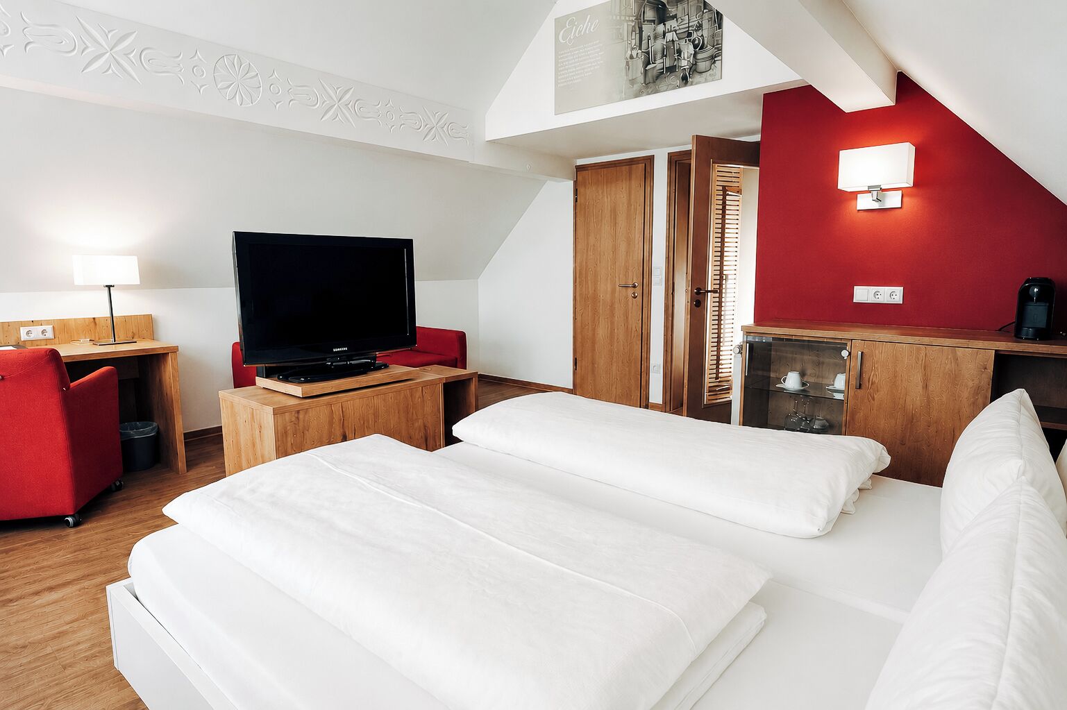 Une chambre d’hôtel avec un lit, un bureau avec une télévision, un mur rouge et une chaise rouge.