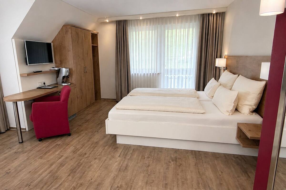 A hotel room with a bed, a desk with a chair, a television, and a wardrobe.