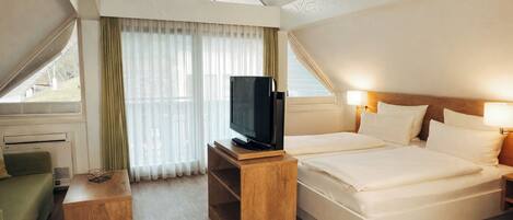 Een hotelkamer met twee bedden, een televisie op een houten standaard, een kleine tafel en een raam met gordijnen.