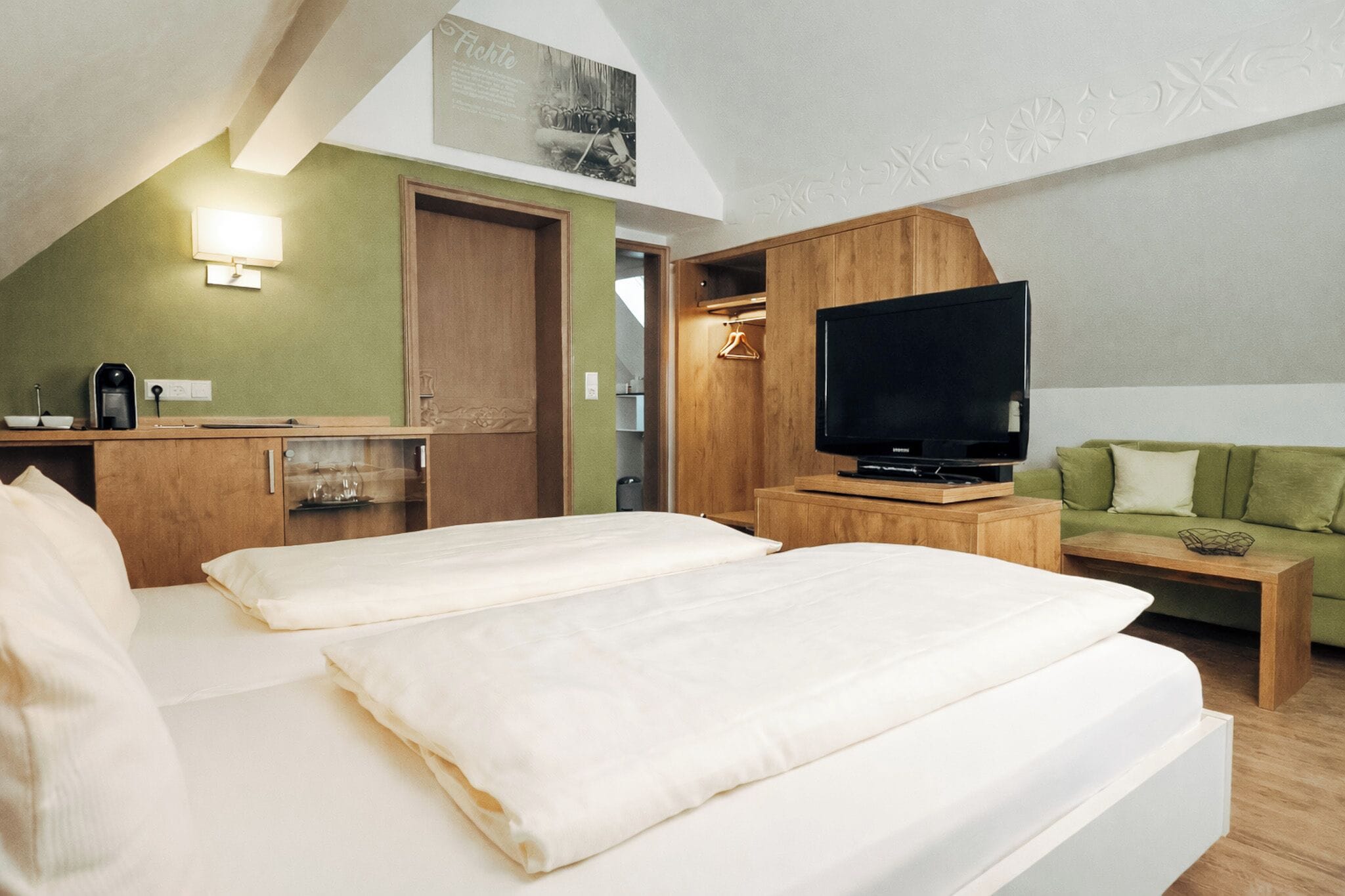 Habitación de hotel con dos camas, televisión, kitchenette y sofá verde.