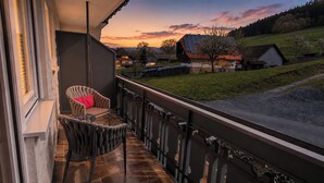 A balcony with a chair, a view of a rural landscape, and a building with a sloped roof. - Hotel Garni Bergblick (Biberach)