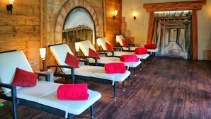 A spa room with multiple white lounge chairs, red towels, and a stone fireplace. - Hotel Garni Bergblick (Biberach)