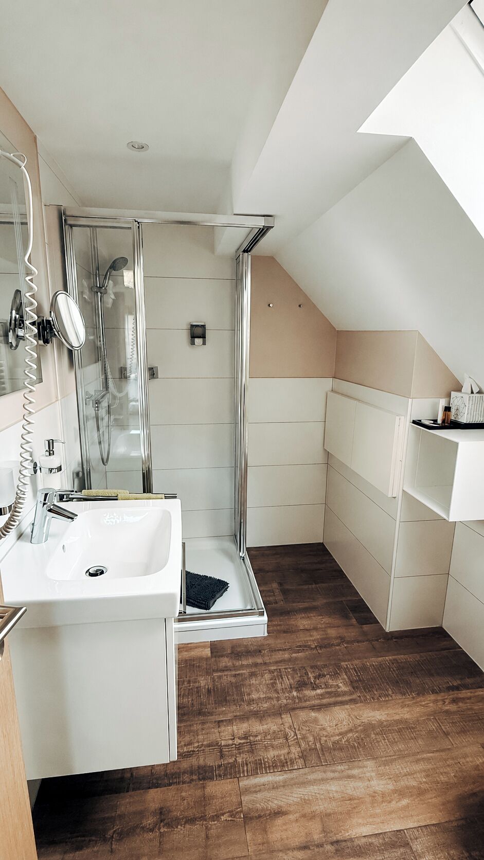 A modern bathroom with a glass shower enclosure, a sink, and wooden flooring.