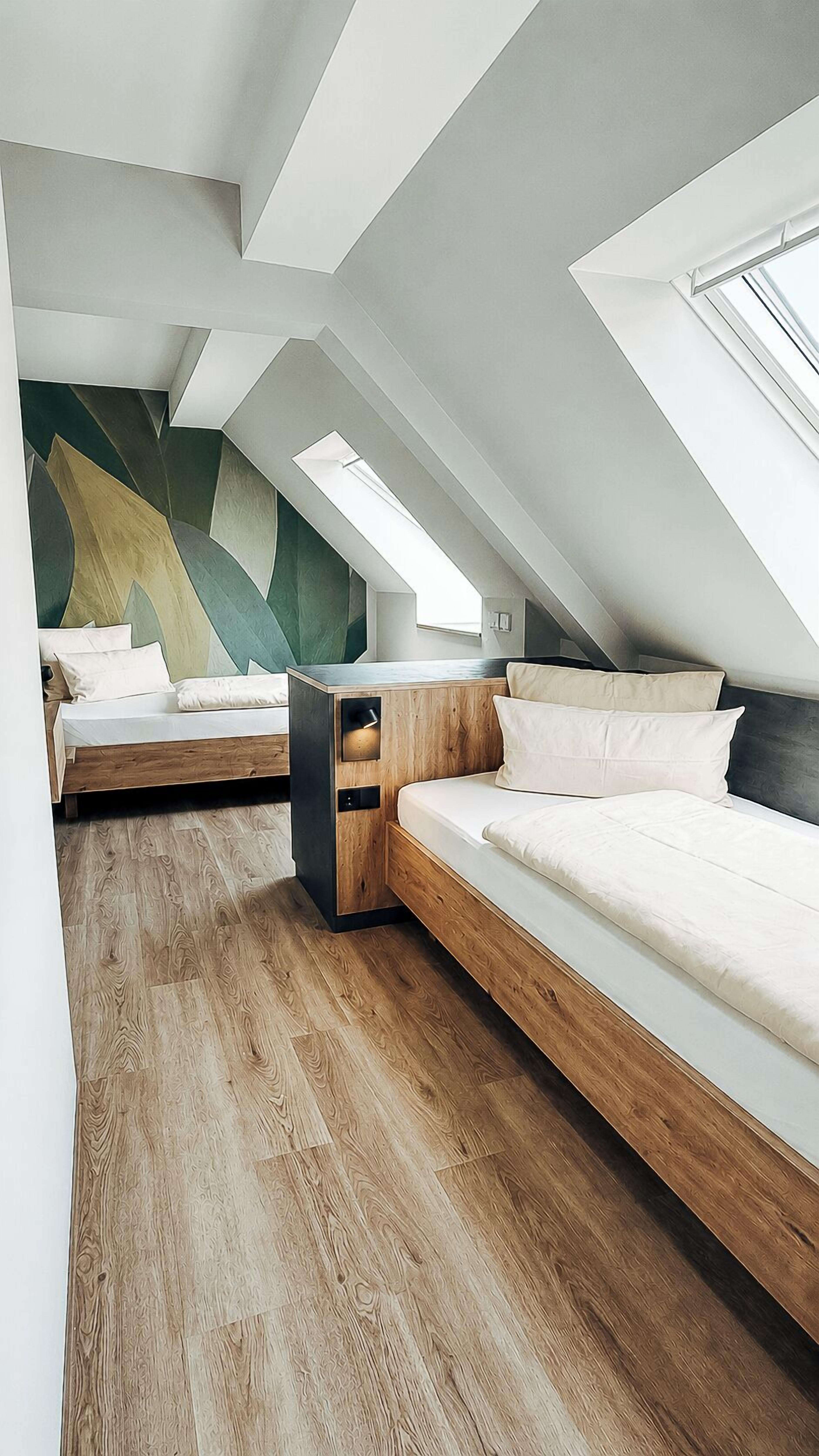 A modern loft bedroom with two beds, wooden flooring, and a geometric wall design.