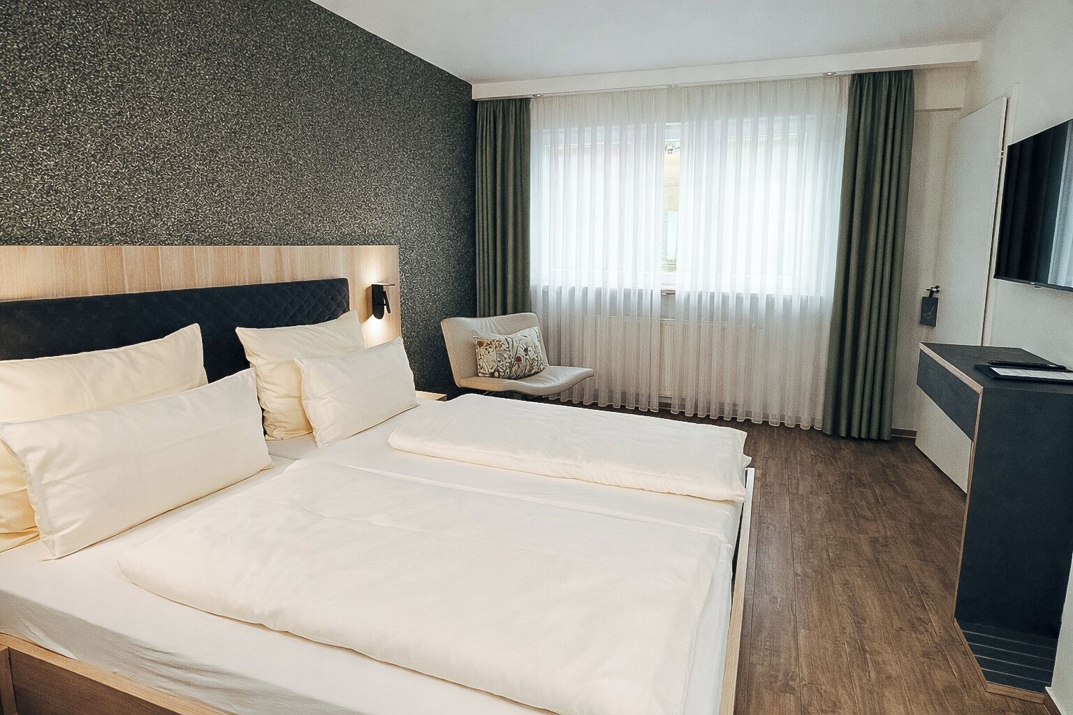 A hotel room with a large bed, a desk, a chair, and a window with curtains.
