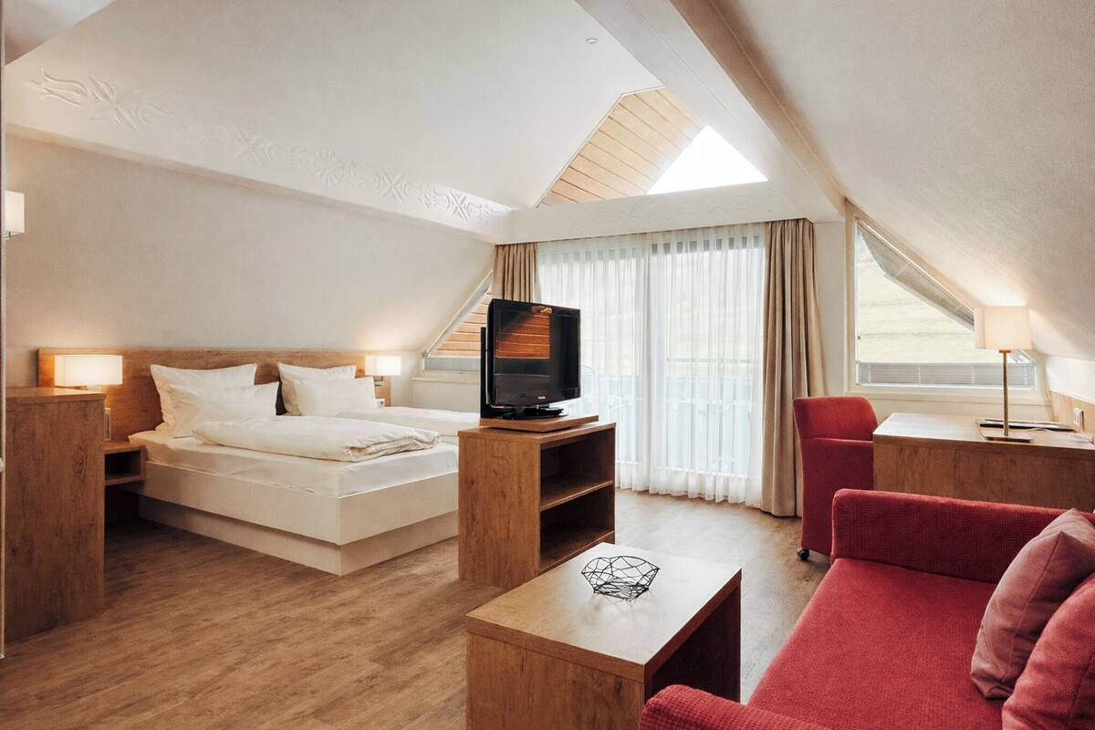 A modern hotel room with a bed, a TV, a red sofa, and a wooden coffee table.