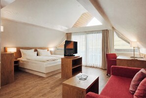 Una habitación de hotel moderna con una cama, un televisor, un sofá rojo y una mesa de centro de madera.