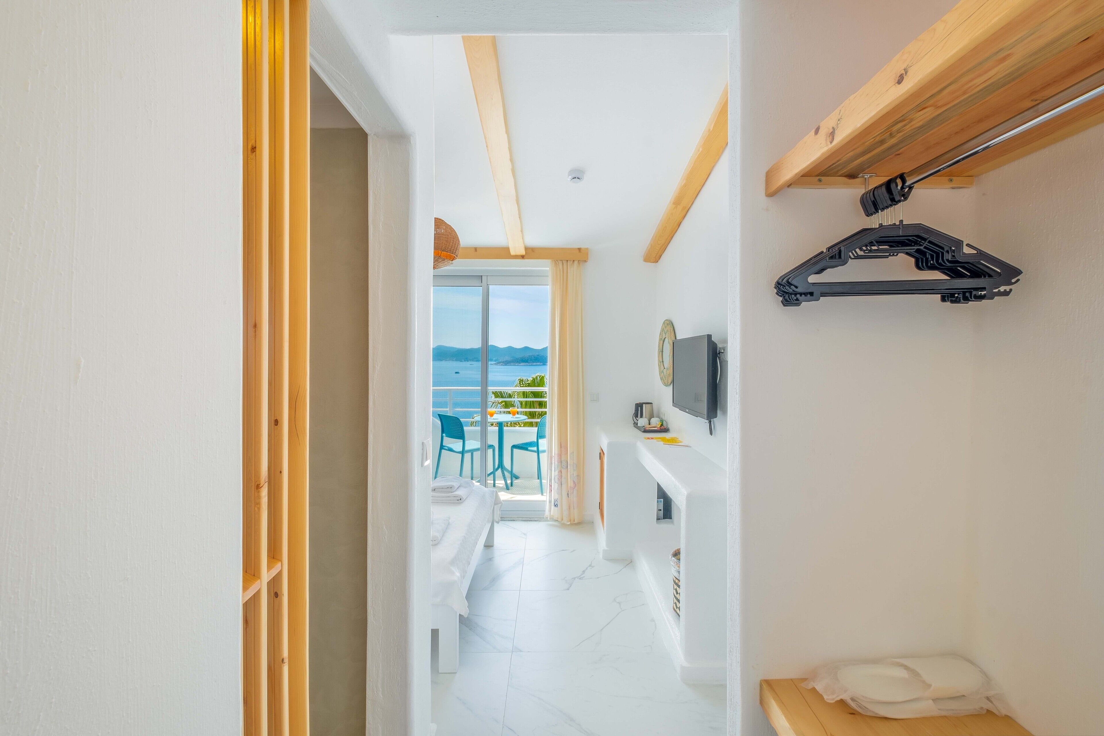 A hotel room with a balcony, a TV mounted on the wall, and a wooden ceiling.