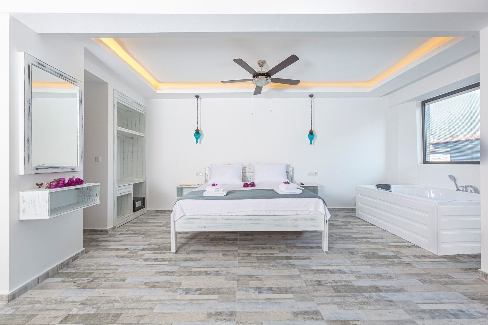 Un dormitorio con cama, mesitas de noche, tocador y un ventanal grande.