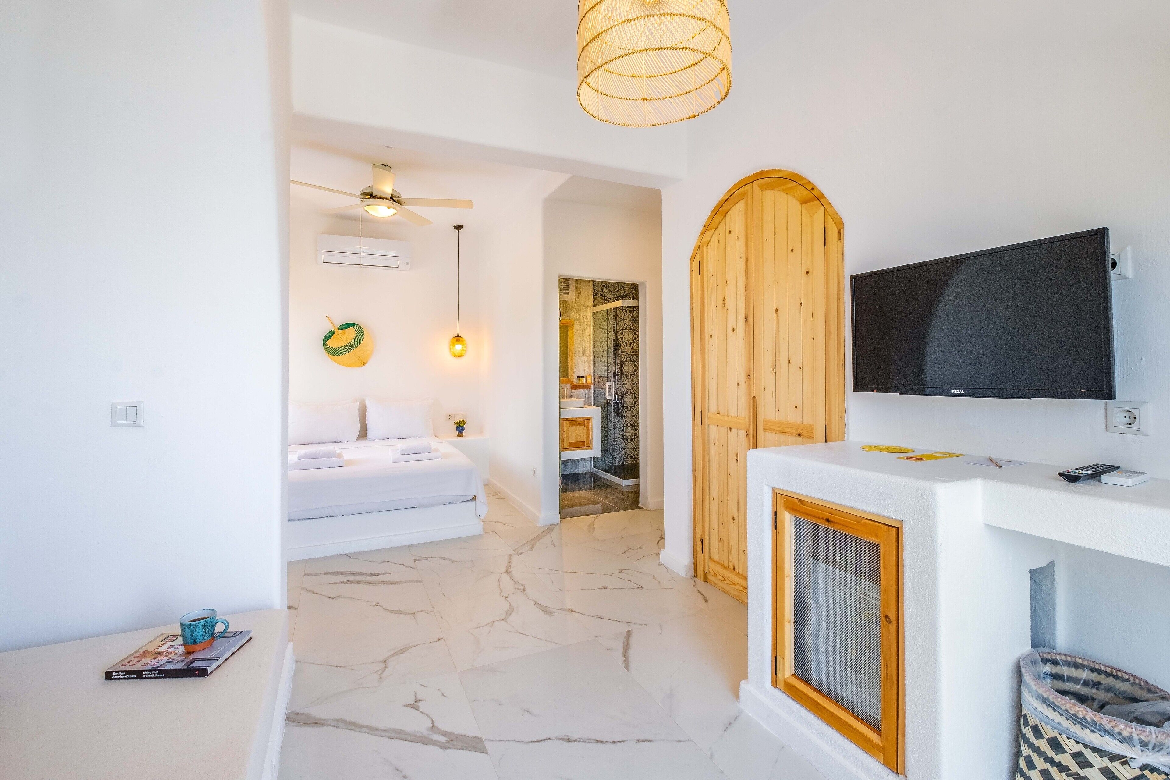 Un baño moderno con un tocador blanco, un televisor montado y una puerta de madera.