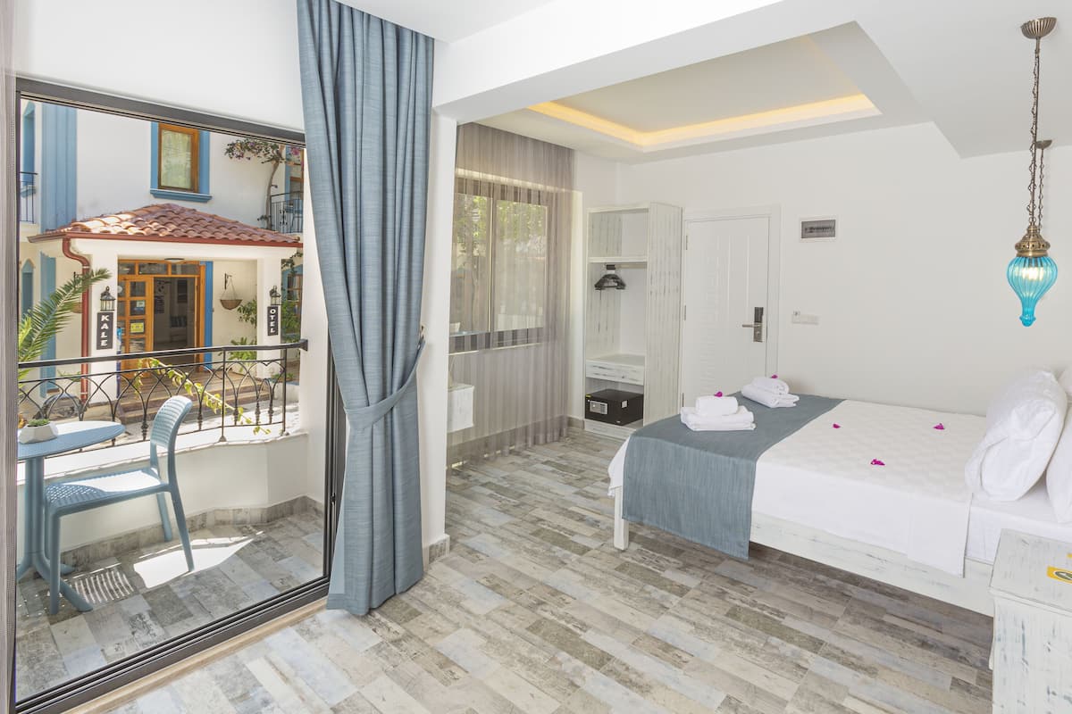 A hotel room with a balcony, a bed with white bedding, a small desk, and a wardrobe.
