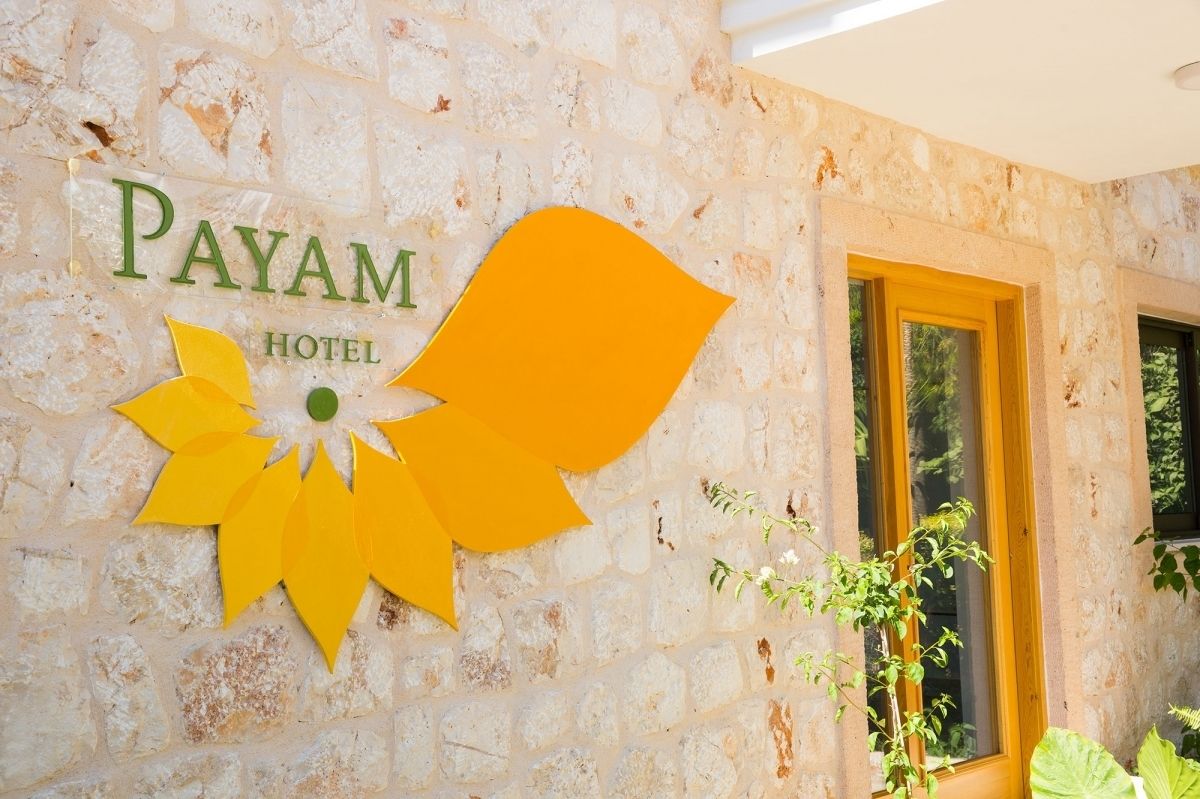 A stone wall with the text "PAYAM HOTEL" and a stylized yellow flower design.