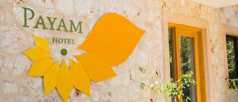 Un mur de pierre sur lequel on peut lire l’inscription « PAYAM HOTEL » et qui est orné d’un motif floral jaune stylisé.