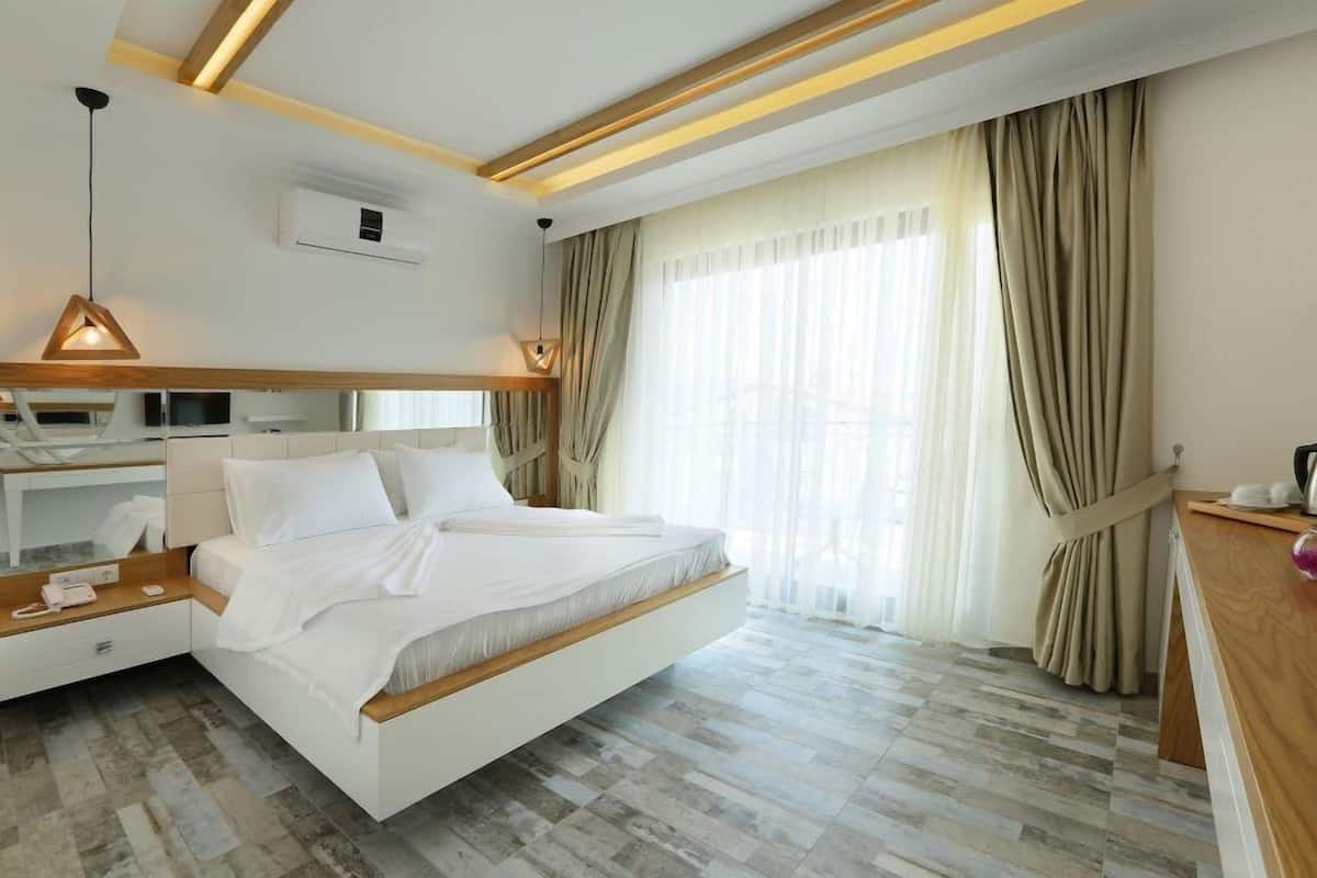 A modern hotel room with a large bed, a wooden desk, a vanity, and a large window with curtains.