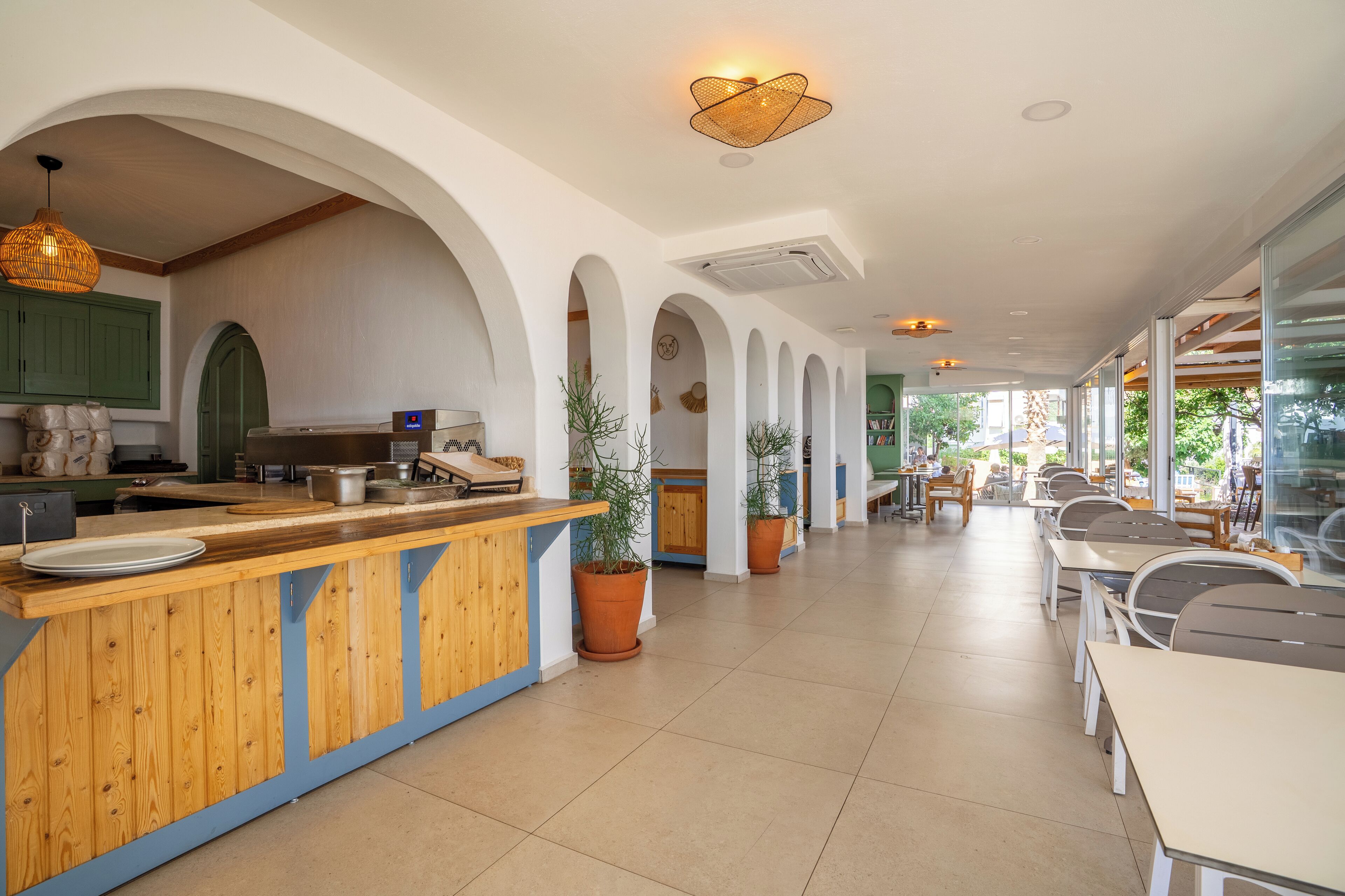 Un restaurante con mostrador de madera, columnas arqueadas y plantas en macetas.