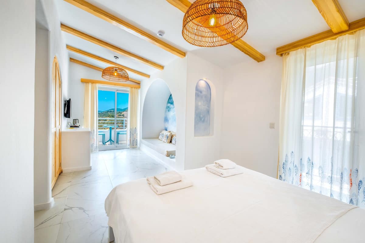 A modern hotel room with a large bed, a balcony with a view, and a wooden ceiling.