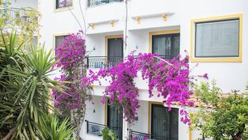 Un immeuble à plusieurs étages doté de balcons, d’un rez-de-chaussée pavé de pierres et agrémenté de plantes en fleurs.
