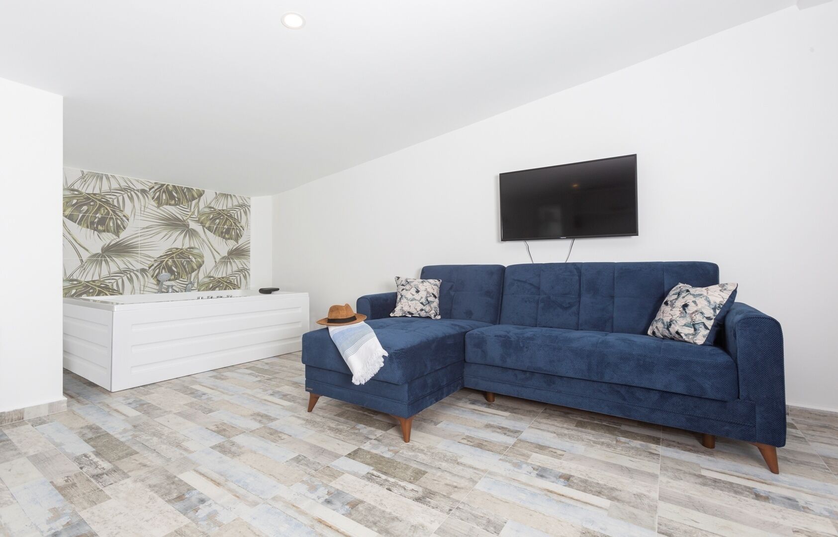 A modern living room with a blue sectional sofa, a white dresser, and a large flat-screen TV mounted on the wall.
