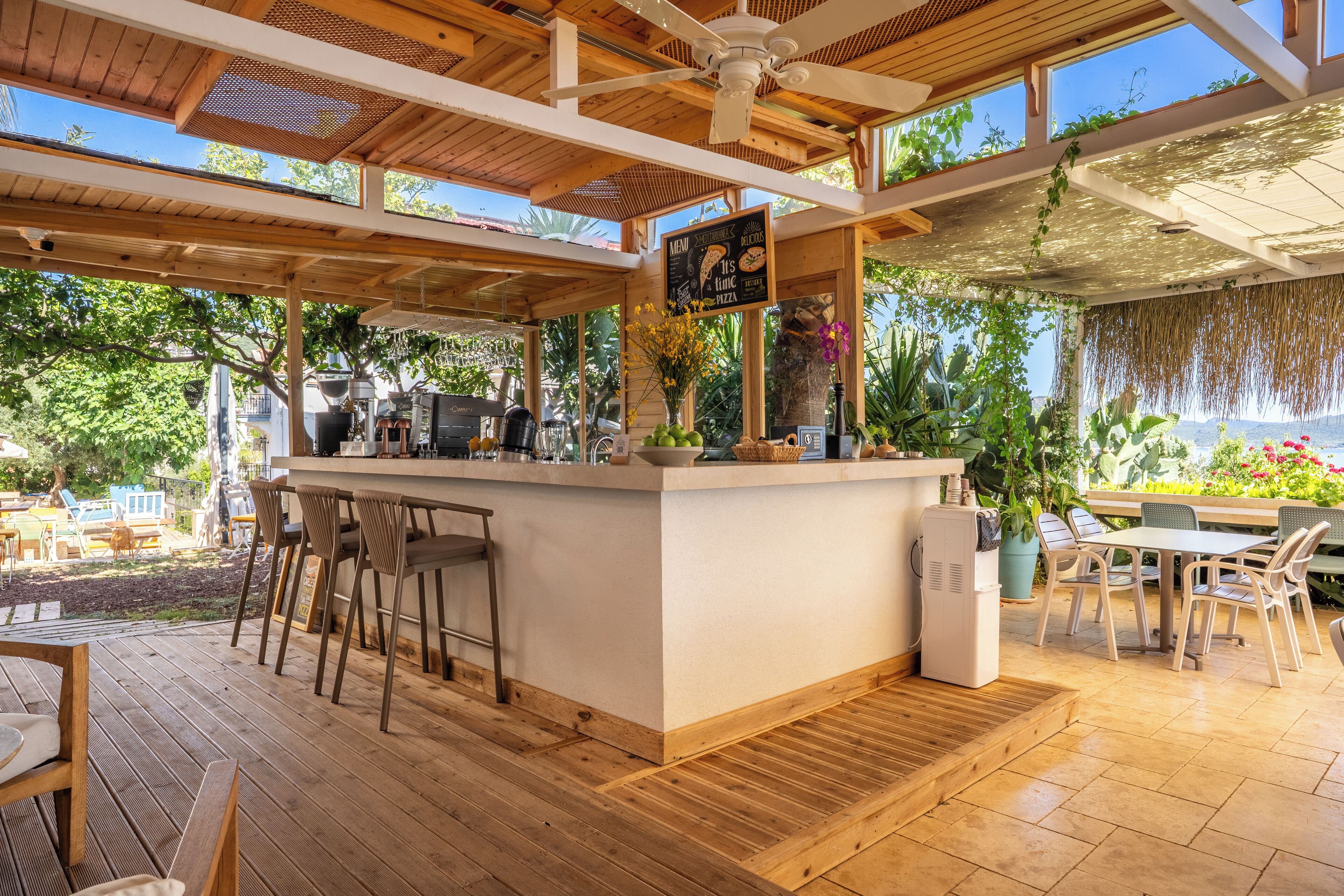 A wooden bar area with a menu sign, outdoor seating, and a view of the garden.