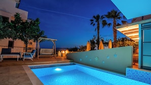 En swimmingpool med kakelbeklädd kant, omgiven av solstolar och en pergola.