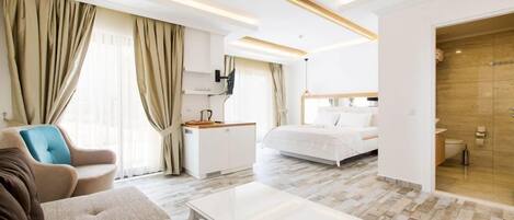 A hotel room with a bed, a sofa, a coffee table, a desk, and a bathroom with a shower.