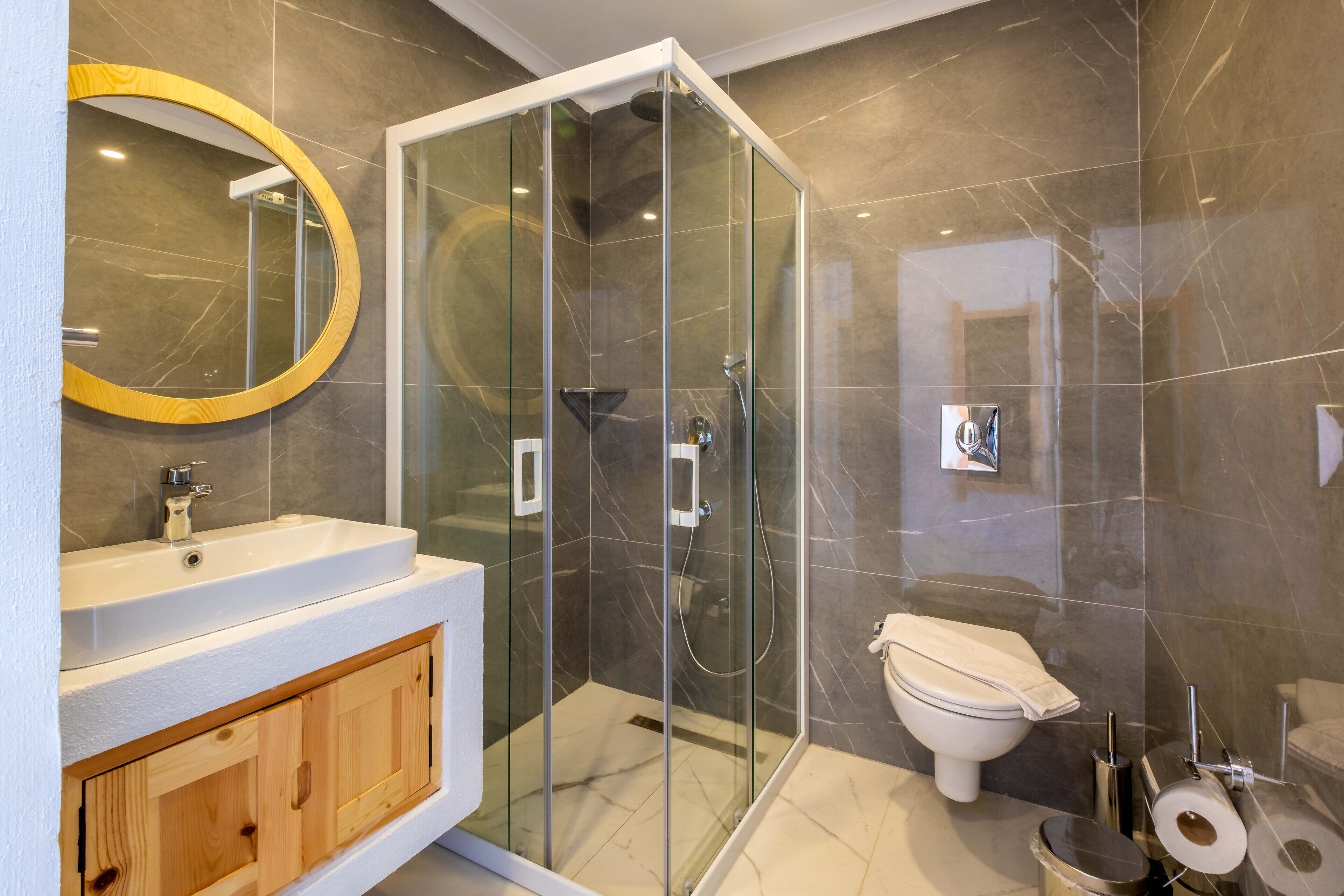 A modern bathroom with a glass-enclosed shower, a white sink, and a wooden vanity.