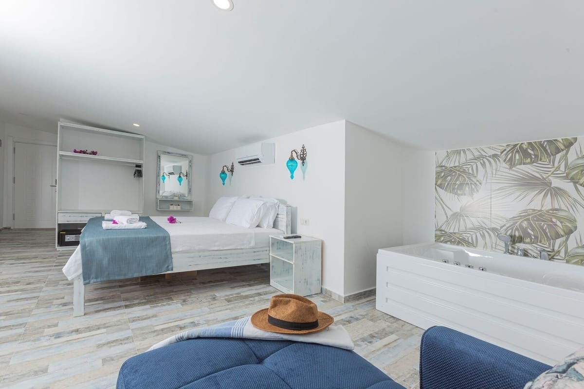 A modern bedroom with a bed, a vanity with a mirror, a dresser, and a wall with tropical wallpaper.