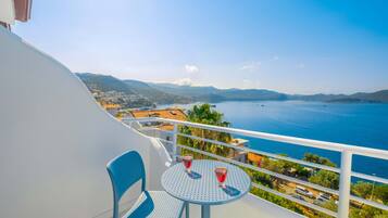 A balcony with a round table and two chairs, overlooking a coastal view with mountains and a body of water.
