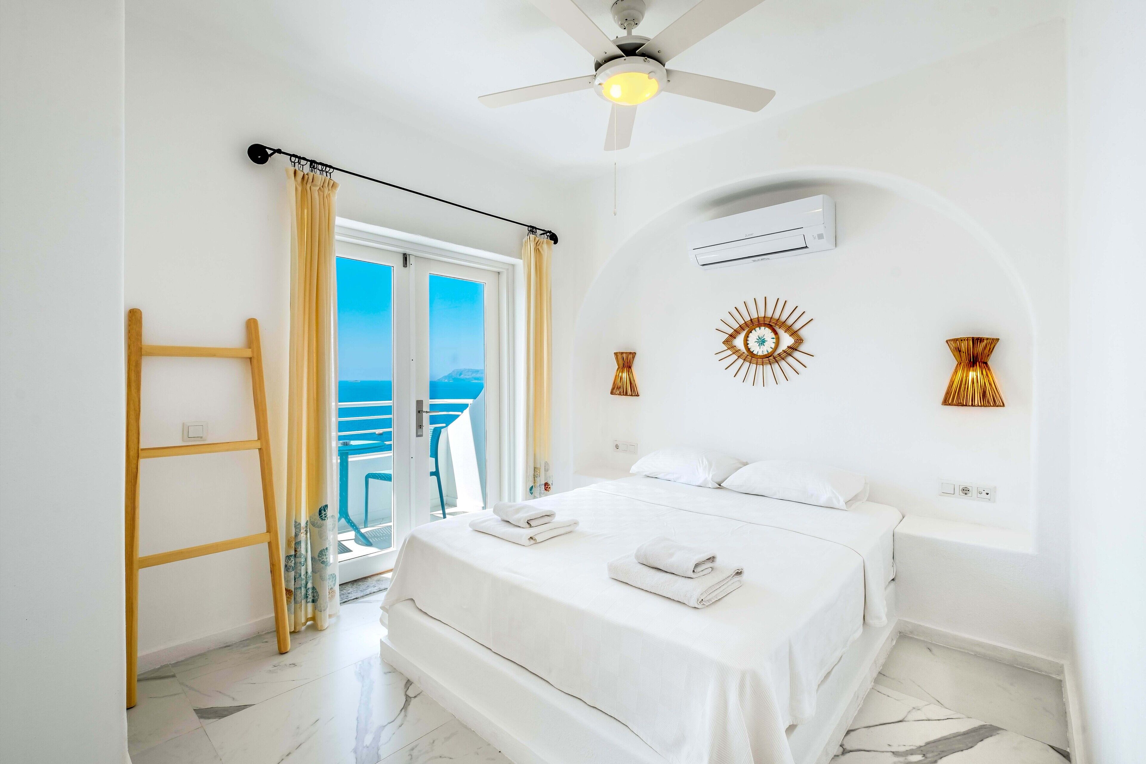 Een hotelkamer met een bed, een plafondventilator, een airconditioning en uitzicht op zee.