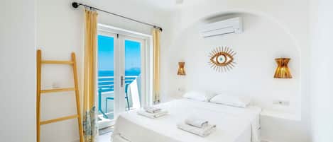 A hotel room with a bed, a ceiling fan, an air conditioning unit, and a view of the sea.