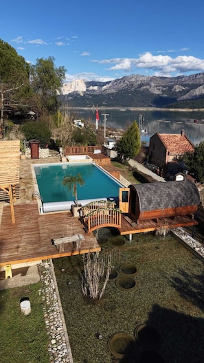 Un área de piscina con cubierta de madera, una sauna y vistas a un lago y montañas.