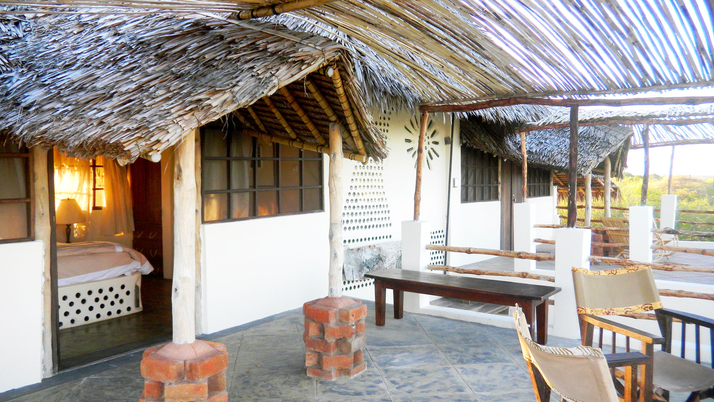 A thatched-roof hut with a bed, a table, and chairs.