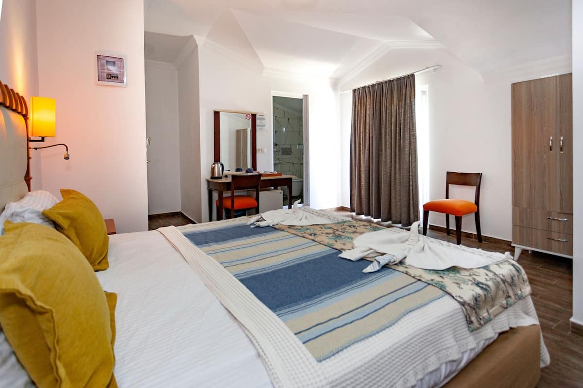 A hotel room with a bed, a desk, a chair, a wardrobe, and a bathroom visible through an open door.