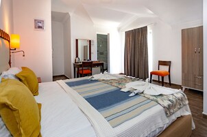 Habitación de hotel con cama, escritorio, silla, armario y baño visible a través de una puerta abierta.