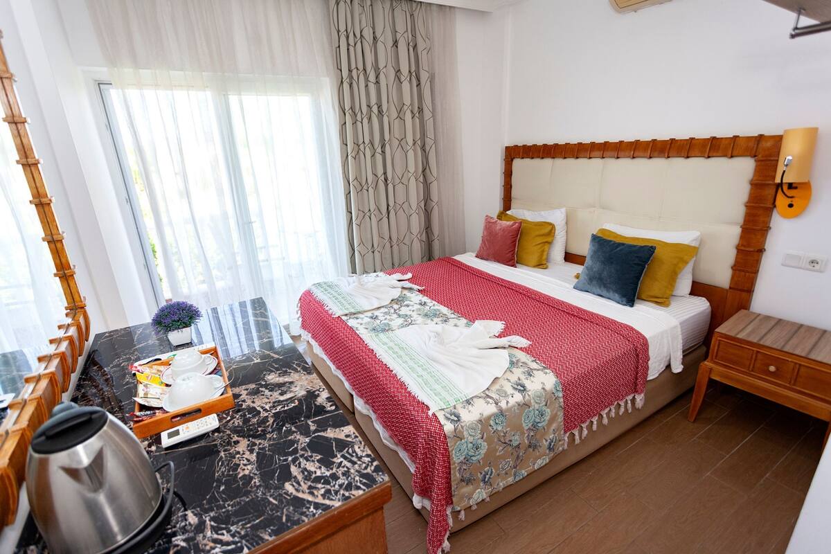 A hotel room with a bed, bedside table, and a window with curtains.