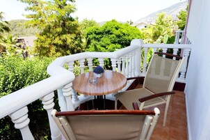 Varanda com mesa de madeira redonda e duas cadeiras, rodeada por vegetação exuberante e paisagem montanhosa.