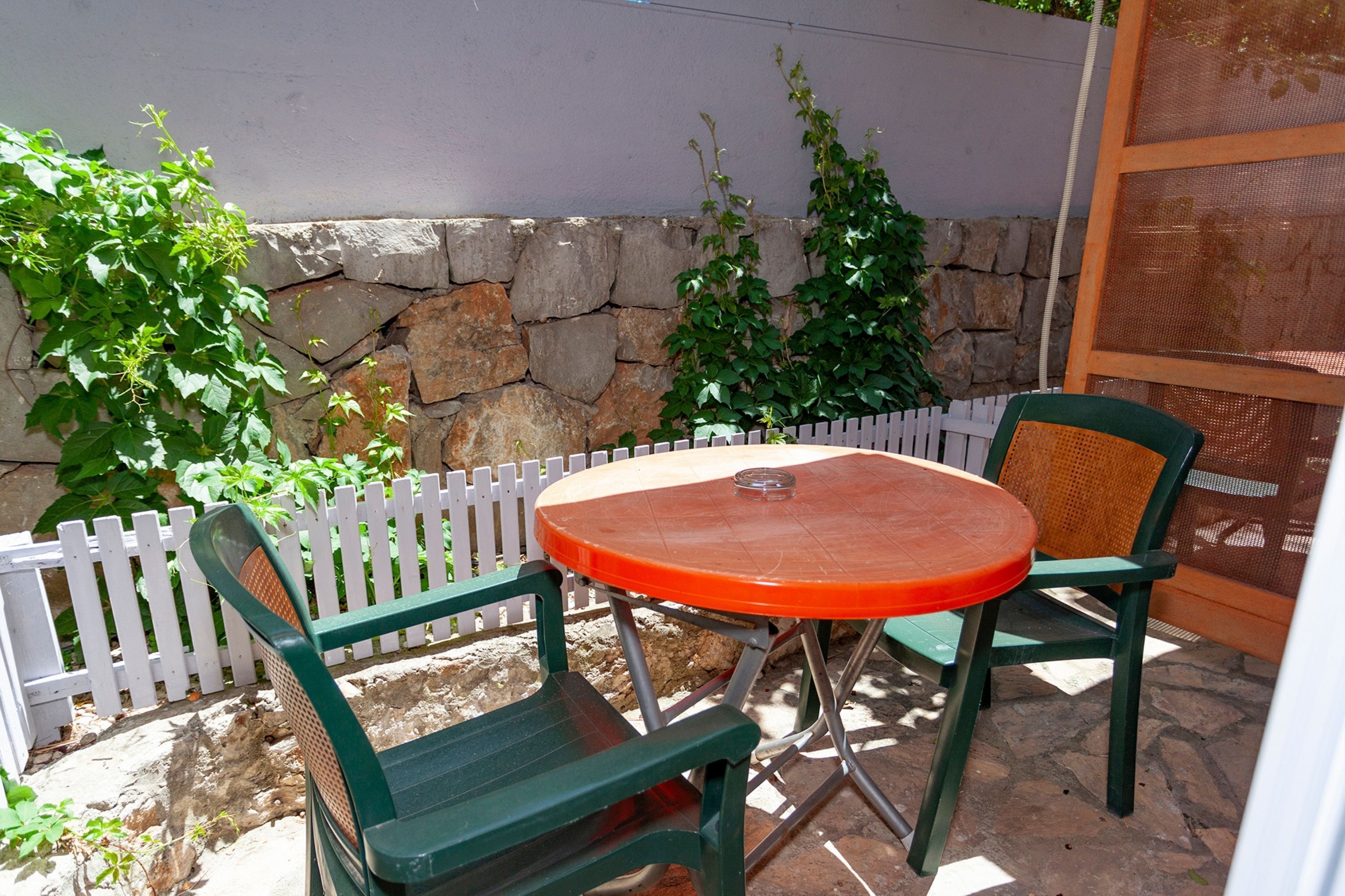 An outdoor patio with a round table and two chairs, a white picket fence, and a stone wall.